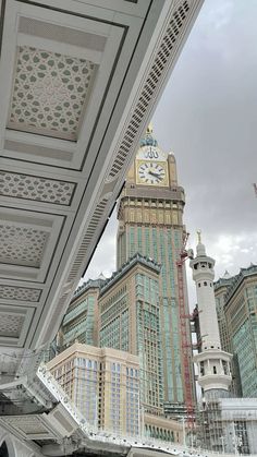 a clock tower in the middle of a city with tall buildings behind it and a cloudy sky