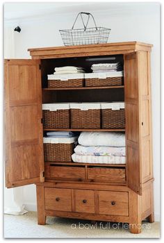 an armoire with baskets and linens in it