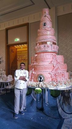 a man standing next to a large pink cake