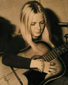 a woman with long blonde hair is playing the guitar and looking down at her wrist