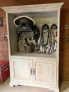 a white cabinet with horse riding gear on top and other items in the back ground