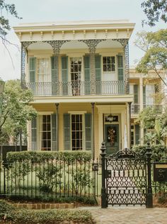 a large yellow house with green shutters on the front and side doors, surrounded by trees