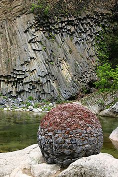 a large rock sitting on top of a river next to a lush green forest