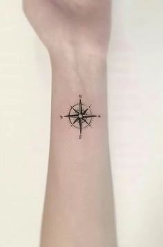 a small wrist tattoo with a compass on the left side of the arm and an arrow in the middle