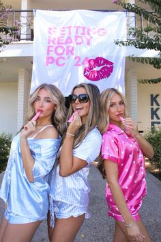 three beautiful young women standing next to each other in front of a white sign with lipstick on it