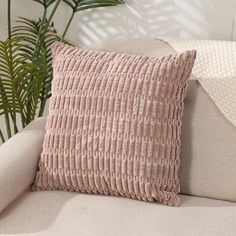 a pink pillow sitting on top of a couch next to a plant