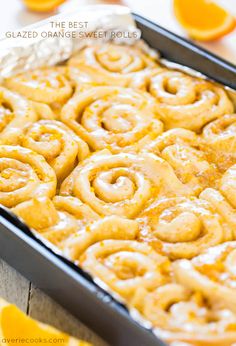 orange sweet rolls in a baking pan on a table with sliced oranges around them