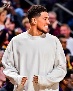 a young man wearing a white sweatshirt standing in front of a crowd at a basketball game