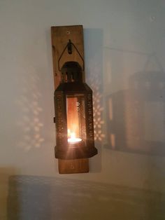 a wall mounted light fixture with a candle lit in the center and shadows on the wall behind it