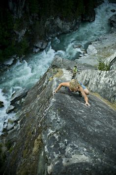 a woman climbing up the side of a cliff next to a river