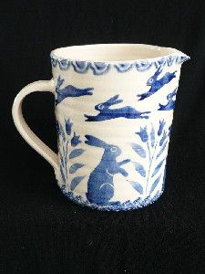 a blue and white cup with rabbits on it's side, sitting on a black surface