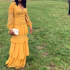 a woman in a long yellow dress standing in the middle of a field with two people behind her