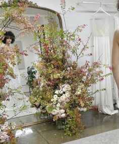 a woman standing in front of a mirror next to flowers