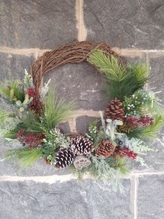 a wreath with pine cones and evergreens on a stone wall next to a brick wall