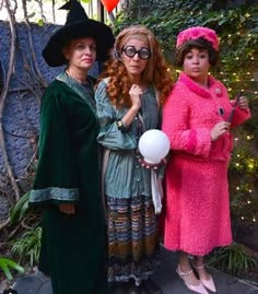 three women dressed in costumes standing next to each other with balloons and trees behind them