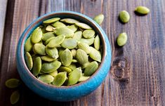 a blue bowl filled with pistachios on top of a wooden table