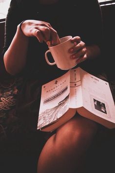 a woman sitting on a couch reading a book and holding a coffee cup in her hand