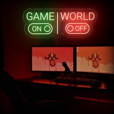 two computer monitors sitting next to each other in front of a neon sign that says game world on off