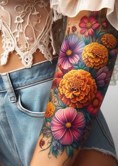 A marigold and cosmos birth flower tattoo intertwines passion and peace. Ideal for those who appreciate the beauty of both flowers. Pretty Floral Sleeve Tattoo, Marigold Flower Tattoo Sleeve, Embroidery Tattoo Flower, Flower Tatoos Woman Arm, Sleeve Tattoos For Women Colorful, Cosmos And Marigold Tattoo, Cosmo And Marigold Flower Tattoo, Watercolor Flowers Tattoo, Colored Flowers Tattoo