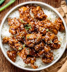 a white bowl filled with chicken and rice on top of a wooden table next to chopsticks