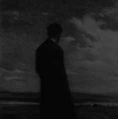 a black and white photo of a man standing in front of the ocean with clouds