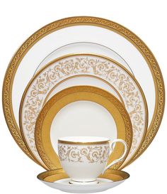 the gold and white dinnerware is set with an ornate design on it's side