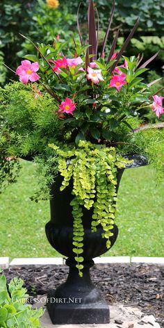 a black vase filled with flowers and greenery on top of a stone slab in the middle of a garden