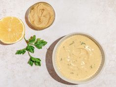 a bowl of dip next to two slices of lemon and parsley on a white surface