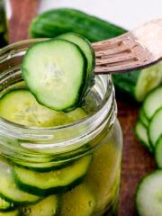 a jar filled with pickles sitting on top of a wooden table next to cucumbers