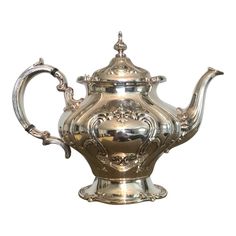 a silver tea pot with ornate designs on the top and sides, sitting in front of a white background