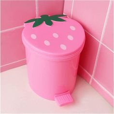 a pink plastic container with a green leaf on the lid next to a tiled wall