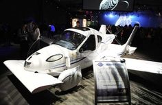 a small white airplane on display at an event with people around it and a screen in the background