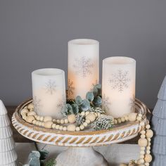 three white candles sitting on top of a tray with snowflakes and pine cones