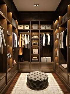 a large walk in closet with lots of clothes on the shelves and an ottoman underneath