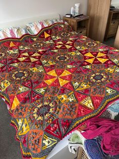 a bed with a colorful blanket on top of it next to a dresser and drawers