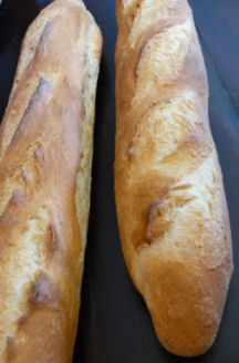 two long loafs of bread sitting next to each other on a black table top