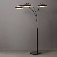 three light floor lamp with black metal base and four lights on each side, against a gray wall