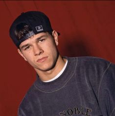 a young man wearing a black hat posing for a photo in front of a red wall