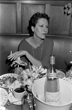 a black and white photo of a woman sitting at a table with food in front of her