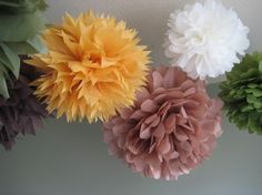 four different colored paper flowers hanging from the ceiling in front of a white wall with green leaves on it