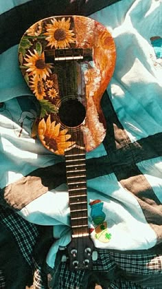 an acoustic guitar with sunflowers painted on it sitting on a quilted blanket