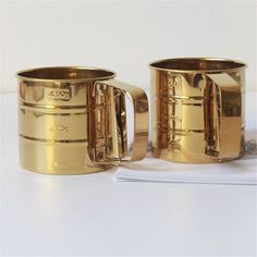 two gold mugs sitting next to each other on a table