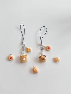 four different shaped earrings with charms attached to each other on a white surface, one has a teddy bear and the other has cookies