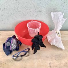 a red bowl sitting on top of a wooden table next to sunglasses and other items