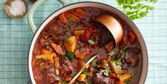 a pot filled with stew and vegetables on top of a green table cloth next to spoons