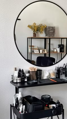 a round mirror hanging on the wall above a shelf filled with makeup and other items