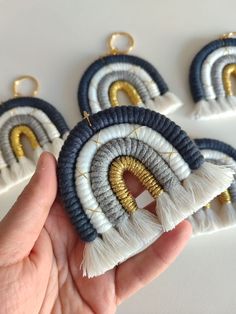 hand holding four different colored tassels with gold and silver details on them, in front of a white background