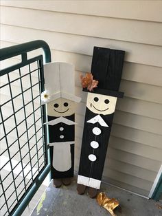 two wooden peg dolls are standing next to each other on the front porch, one is wearing a suit and tie