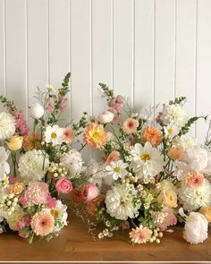 three vases filled with flowers on top of a wooden table in front of a white wall