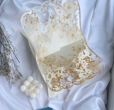 a white and gold tray sitting on top of a bed next to some dried flowers